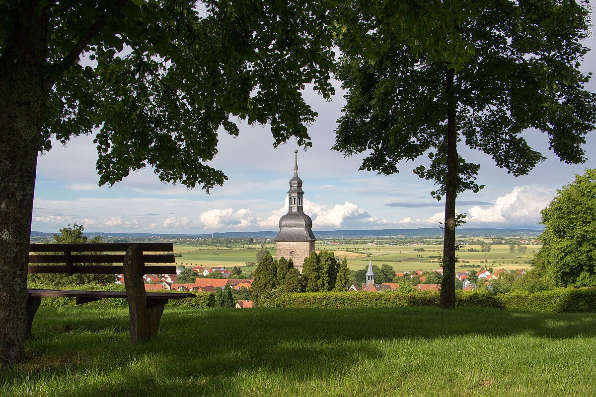 Ortsansicht (Burgbernheim, Romantisches Franken) Bank unter Bäumen mit Blick auf Kirchturm und Dorf in ländlicher Umgebung bei Tageslicht